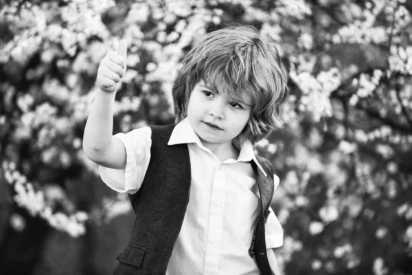 Ano ty. bezstarostný chlapec ukázat palec nahoru. malý chlapec na kvetoucím jarním stromě. Šťastné dítě má svěží zdravé vlasy. letní a jarní móda. dítě si vychutnat kvetoucí přírodu v části. štěstí v dětství — Stock fotografie
