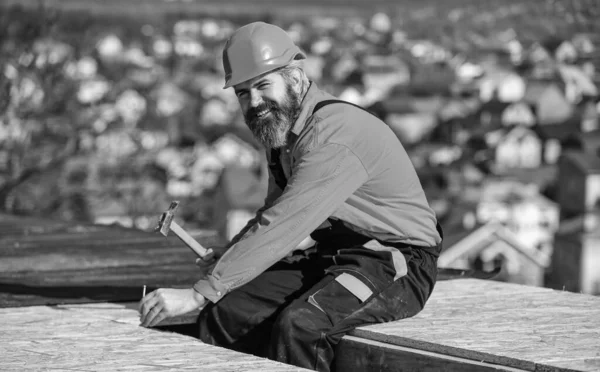 Handsome builder use hammer. professional master repair roof. Flat roof installation. roofing felt. Roofer worker in special protective work wear. new roof under construction residential building — Stock Photo, Image