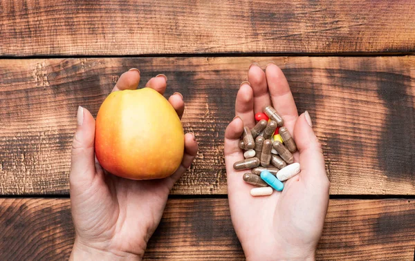 Alimentos naturales de manzana y suplementos dietéticos en cápsulas en manos femeninas fondo de madera, vitaminas —  Fotos de Stock