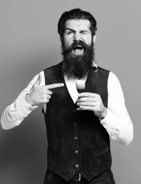 Uzun sakallı ve bıyıklı yakışıklı bir adam elinde bir bardak alkolle klasik süet deri yelek giymiş kırmızı stüdyo arka grubunda.