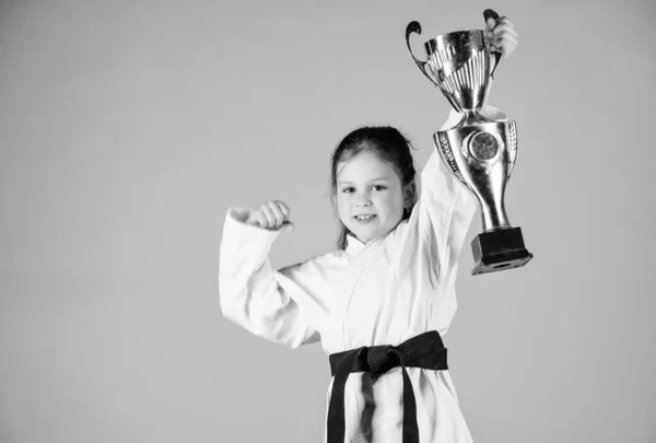 Sport success in single combat. practicing Kung Fu. happy childhood. winner little girl in gi sportswear. small girl with champion cup. martial arts. energy and activity for kids. Striking the pose — Stock Photo, Image