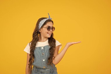 Retro kız ürünü sunuyor. Küçük çocuklar yaz kıyafeti giyer. Neşeli çocuğun klasik bir görünüşü var. Mendil ve güneş gözlüğü - yaz aksesuarı. Güzellik ve moda. Mutlu çocukluk. Boşluğu kopyala