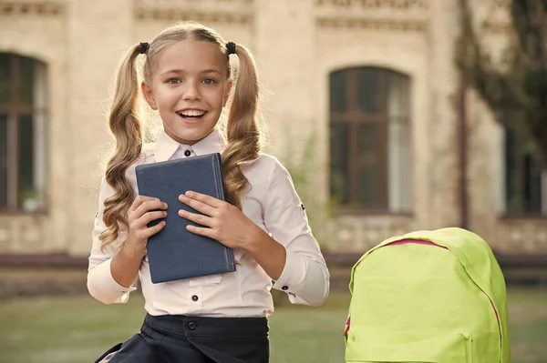 Mała dziewczynka trzyma książkę. literatura dla dzieci. rozwój dzieciństwa. Pracuj z notatnikiem. Z powrotem do szkoły. Dzieciak z torbą szkolną. Uśmiechnięte dziecko z plecakiem. Odrabiajmy lekcje. — Zdjęcie stockowe