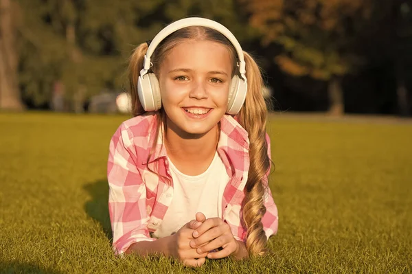 Nueva tecnología para los niños. recuerdos de la infancia feliz. escuchando música. de vuelta a la escuela. Estudiar en Park. relajarse en la hierba verde en los auriculares. niña pequeña escuchar audio libro — Foto de Stock