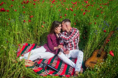 Gitarlı aşıklar çiçek tarlasında şarap içerler. Müzik. Birbirine aşık çiftler. Gelincik tarlasında kadın ve erkek.