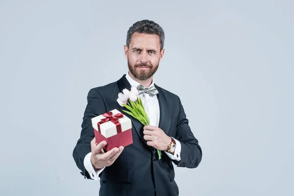 Bonito smoking homem segurar caixa de presente e tulipa flores, aniversário — Fotografia de Stock