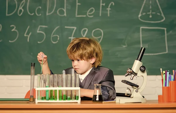Vetenskapligt koncept. Ett begåvat barn och en tvättbjörn. En lektion i kemi för barn. Skolutbildning. Pojken använder mikroskop och provrör i klassrummet. Ett geni-barn. Kemisk analys — Stockfoto