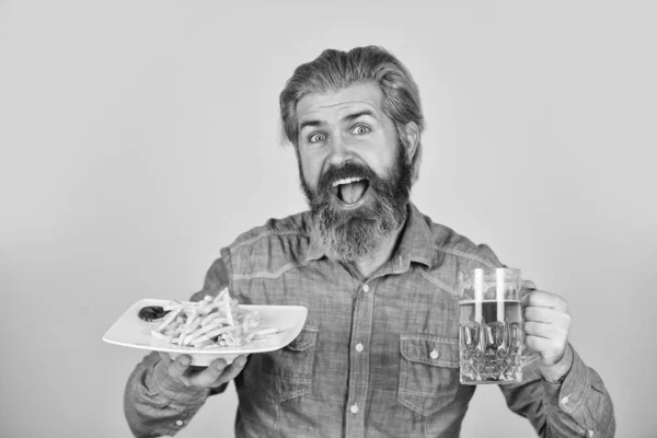 Cerveja e comida. Desfrute de futebol na TV. Batatas fritas perfeitas. Consumir álcool. Assista jogo desportivo no pub. O homem bebe cerveja e come lanches. Restaurante Bar. Homem alegre barbudo hipster bebendo cerveja — Fotografia de Stock