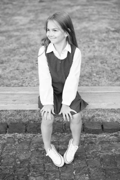 Ευτυχισμένο κοριτσάκι με επίσημη σχολική στολή κάθισε στο παγκάκι του πάρκου, μαθήτρια — Φωτογραφία Αρχείου