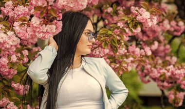 Sakura ağacı çiçek açıyor. Yumuşak ve yumuşak. Sakura ona yakışıyor. Muhteşem çiçek ve dişi güzellik. Bahar çiçeğinin açtığı süslü güneş gözlüklü kadın. Cilt için doğal kozmetik. Kiraz çiçekli kız.