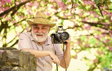 Emeklilik gezisi. Çekici güzellik. Çiçek açan bahçede fotoğrafçı. Kıdemli adam profesyonel kamerayı tutuyor. Fotoğraf kursları. Seyahat ve turizm. Mutlu büyükbaba. Bahar tatili. Seyahat fotoğrafı.