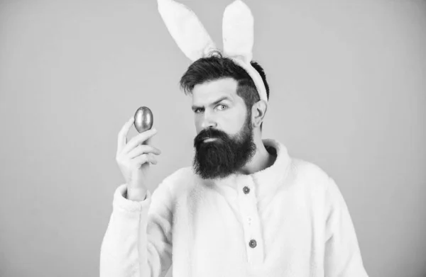 Wielkanoc. Hipster noszący długie królicze uszy z jajkiem wielkanocnym. Pisanka jest symbolem nowego życia i zmartwychwstania. Człowiek z brodą w stroju królika wielkanocnego trzymający jajko paschalne. Tradycja barwienia jaj — Zdjęcie stockowe