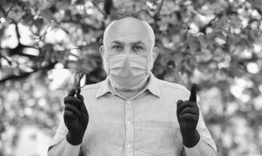 Kurallara uy. Tıbbi maske ve eldiven giymiş kıdemli bir adam. Parktaki sakura ağacı. Coronavirus kapanışı sırasında hayat. Hastalık korkusu. Virüsle savaşma stratejisi. Halka açık yerlerde ziyaret yasağı