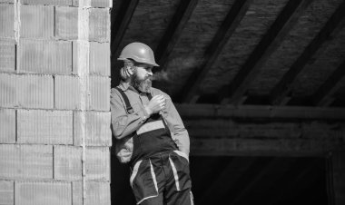 Sigara içen inşaat işçisi. Bina yapım aşamasında. Üniformalı ve kasklı sakallı adam. kopyalama alanı. Tamirci olay yerinde kask takıyor. Yorgun müteahhit. Dinlenme zamanı.