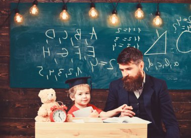 Baba sakallı, öğretmen oğlu, küçük çocuk öğretiyor. Havan tahtasındaki öğretmen ve öğrenci, arka planda yazı tahtası. Bireysel eğitim konsepti. Çocuk evde öğretmeniyle ayrı ayrı çalışıyor.