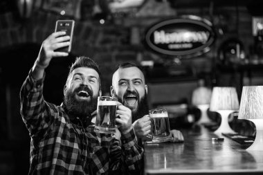 Çevrimiçi iletişim. Sakallı hippi adam akıllı telefon tutar. Selfie konseptini alıyorum. Barda harika bir akşam geçirdiğini hatırlamak için selfie çek. Arkadaşların sosyal ağlarına selfie çek. Barda bira içen bir adam