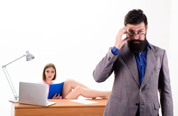 Smart and good looking guy. Smart man looking through glasses with sexy woman working in background. Bearded man in smart casual wear with coworker. Smart businessman and pretty secretary in office — Stock Photo, Image