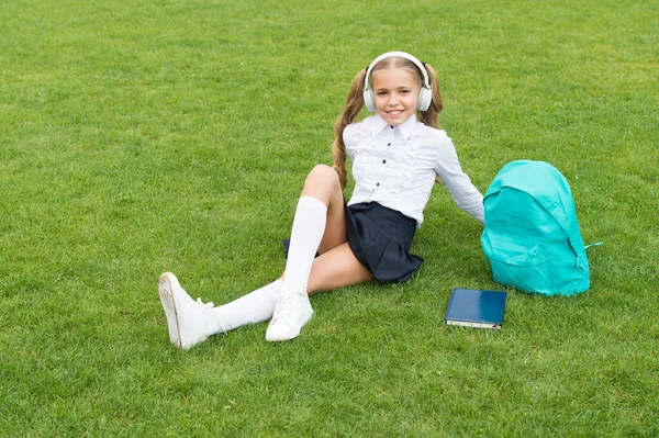 Vacances scolaires. Joyeux enfant en uniforme d'école assis sur l'herbe verte. Passez un bon été — Photo