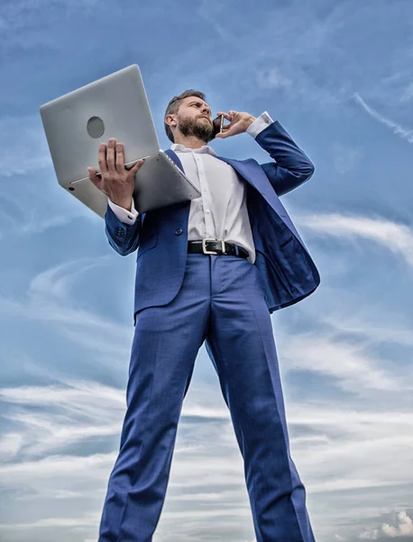 Immer in Kontakt. Mann gepflegten Geschäftsmann hält Laptop, während Telefon blauen Himmel Hintergrund sprechen. Guy formale Anzug moderne Technologie Manager Unternehmer beantworten Telefonanrufe. Geschicklichkeit vermitteln — Stockfoto