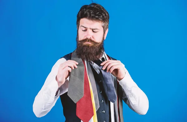 Cómo elegir la corbata correcta. Estilo clásico. Cómo combinar corbata con camisa y traje. Hombre barbudo hipster sostienen pocas corbatas sobre fondo azul. Un tipo con barba escogiendo corbata. Guía de caballeros — Foto de Stock