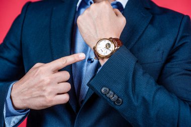 Kıyafetli bir saat takıyordu. Mavi takım elbise ve kol saati erkek elinin kırpık görüntüsünde..