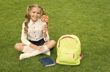 Okula dönüyorum. Komik çocuk lolipop tutuyor. Eğitim konsepti. Sıradan bir öğrenme günü. Şirin kız dersten sonra kitap okuyor. Okul bahçesinde kitabı olan mutlu anaokulu kızı.