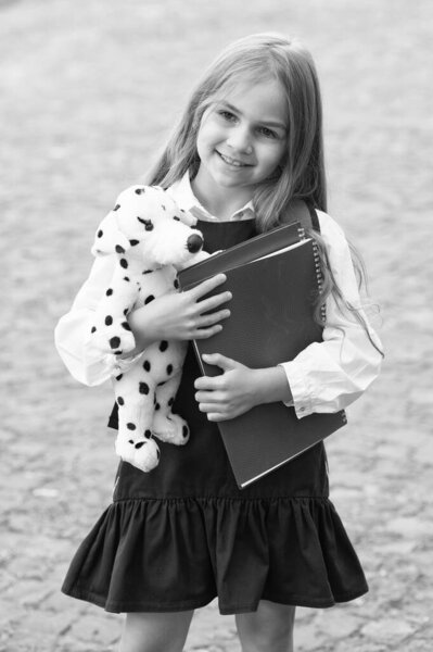 Добавляю веселья в учебу. Счастливый ребенок держит игрушечную собаку и книги на улице. Возвращаемся к школьным принадлежностям. Модная форма. Формальный дресс код. Школьная одежда. 1 сентября. Начальное образование. Больше любите учебу