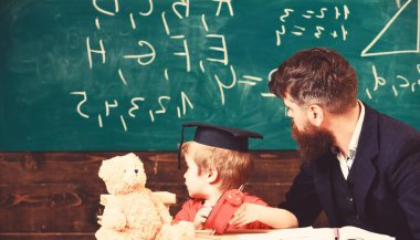 Bireysel ders kavramı. Evlat, öğretmen açıklarken şapkalı çocuk tahtadaki karalamalara bakıyor. Sakallı öğretmen, babası küçük oğluna ders veriyor, arka planda karatahta.