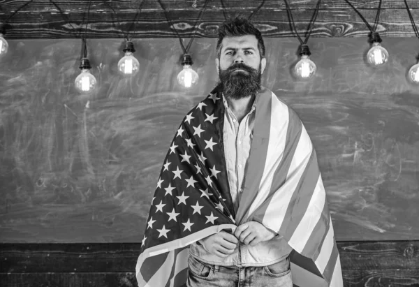 Professor americano coberto com bandeira americana. Homem com barba e bigode no rosto sério com bandeira dos EUA, quadro-negro no fundo. Conceito de educação patriótica. Professor ensina a amar a pátria, EUA — Fotografia de Stock