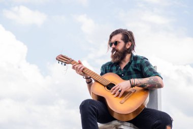 Müziğe benziyor. Uzun saçlı hippi ve bıyıklı gitarist. Müzik aleti olan erkek gitarist. Country müzik konsepti. Sakallı adam akustik gitar çalar. Sıradan bir adam insani duygularını ifade eder.