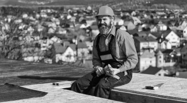 Profesyonel tamir çatısı. Düz çatı kurulumu. Çatı keçesi. Çatı tamircisi koruyucu iş elbisesi giyiyor. İnşaat binasının altındaki yeni çatı. İnşaatçı matkap kullanır. Foreman planlama