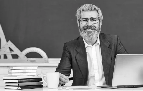 Teacher of year. Elderly man back to school. University professor sit at desk. Bearded man wear formal suit. Happy man with beard and grey hair. Man of science. New technology. School and education