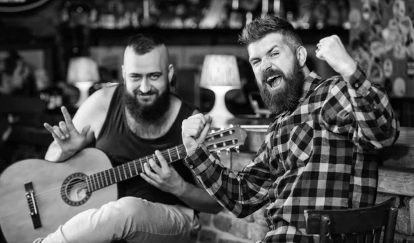 Des amis se relaxent au pub. Concert de musique live. Un homme joue de la guitare dans un pub. Performance acoustique au pub. Hipster barbu brutal avec un ami au pub. Des amis joyeux chantent de la musique de guitare. Relaxation au pub — Photo