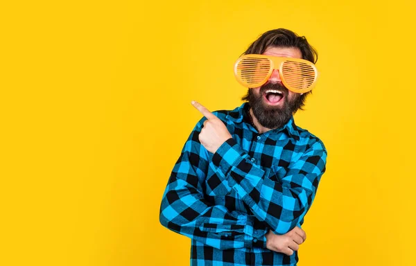 Щасливий бородатий чоловік в смішних партійних окулярах і вказує палець на жовтий фон, копіювати простір, найкраща пропозиція — стокове фото