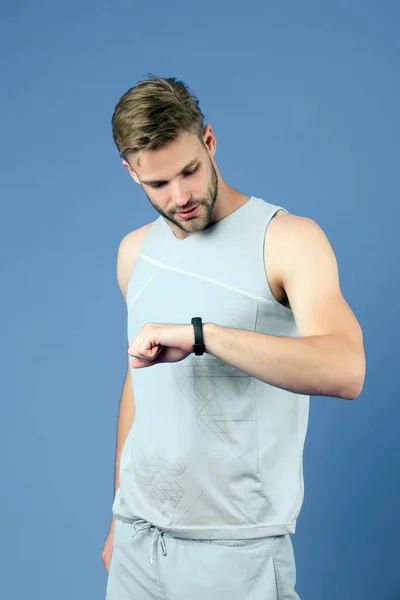 El deportista mira el reloj de fitness sobre fondo violeta. Hombre con reloj inteligente deportivo en ropa deportiva azul. Seguimiento de la actividad y el entrenamiento. Nueva tecnología para un estilo de vida saludable. Deporte o fitness y bienestar — Foto de Stock