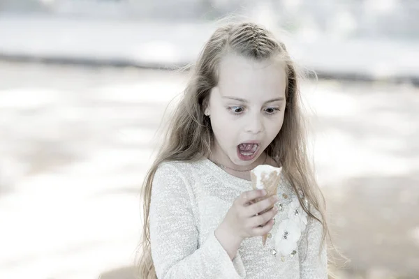 Een meisje met een ijsje in de hand. Summer behandelt concept. Zoet tand meisje kind met wit ijs in wafel kegel. Meisje zoete tand op geschokt gezicht eet ijs, lichte achtergrond — Stockfoto