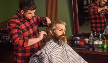 Uzun sarı saçlı adam, yakından bak. Kendi saçını kesme. Hipster müşteri saçını kestiriyor. Makas ve müşteriyle berber. Berber, sakallı adamın berber dükkanı geçmişi için saç stili üzerinde çalışıyor.