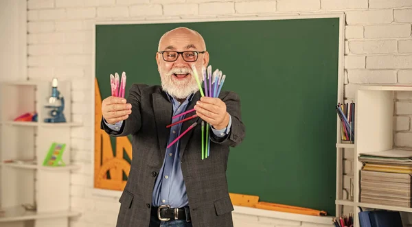 Bunu dene. Okul malzemeleri alışverişi. Adam bir sürü ofis aleti kullanıyor. Kıdemli öğretmen renkli kalem seti tutar. Herhangi bir rengi seç. Mutlu sakallı öğretmen. Okula dönüyorum. Kara tahtalı sınıf — Stok fotoğraf