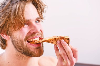 Genç adam evde çıplak ve pizzayla dinleniyor. Yatağında pizza olan gömleksiz genç bir adam. Diyet kimin umurunda. Pizza yatağı.