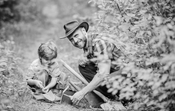 Niño y padre en el fondo de la naturaleza. Herramientas de jardinería. Pasatiempo de jardinería. Papá enseñando plantas para el cuidado de niños. La rutina de jardinería de primavera. Plantando flores. Pequeño ayudante en el jardín. Familia de granja — Foto de Stock