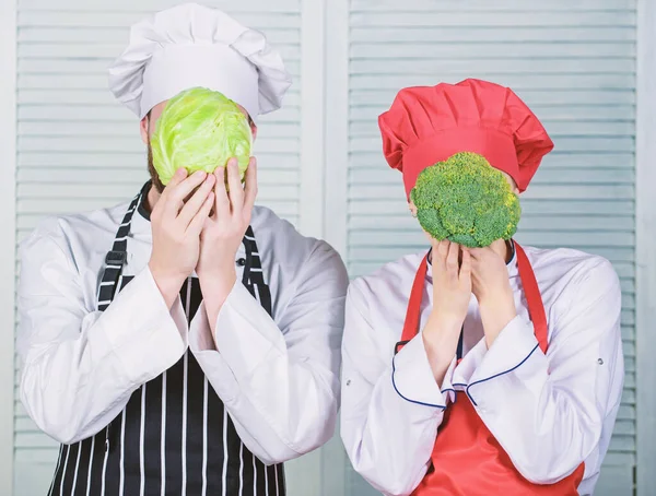 Couple cooks hold cabbage and broccoli in front of face. Healthy food concept. Couple cooking healthy vegetarian meal. Vegetarian family. Vegetarian nutrition and vegetable diet. Diet on their mind