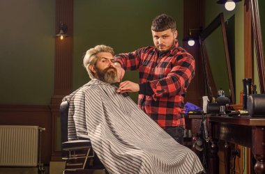 Sakin ve kendinden emin. Berber dükkanında berber aletleri. Yakışıklı kuaför erkek müşterinin saçını kesiyor. Berber dükkanında müşteriye hizmet eden kuaför. Kişisel kuaför. Eski ve eski moda. Tasarım saç kesimi