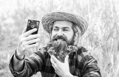 Saf duygular. Telefonda leylakla çekilmiş yaz selfie 'si. Çiftlik hippisinin uzun ve sağlıklı sakalı var. Saçlı çiçek. Hasır şapkalı rahat bir çiftçi. Yetişkin bahçıvan yeşil çimlerde rahatlar. Bahar doğasının tadını