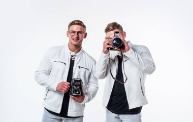 İkiz kardeşler, beyaz giysili fotoğrafçı. Klasik fotoğraf makinesi kullanıp fotoğraf çekiyorlar..