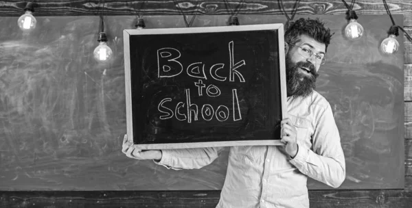Start of school year concept. Teacher on cheerful face holds blackboard with title back to school. Man with beard welcomes students, chalkboard on background. Teacher peeking out of chalkboar — Stock Photo, Image