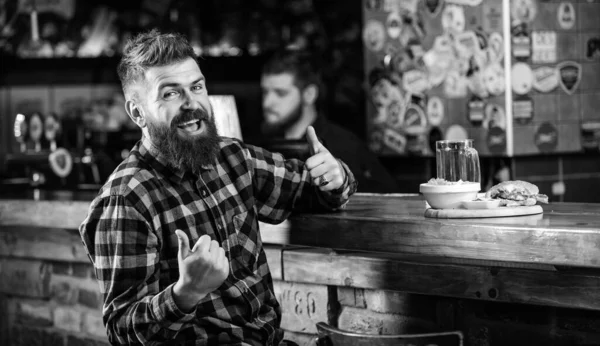 Enjoy meal in pub. High calorie snack. Hipster relaxing at pub. Pub is relaxing place to have drink and relax. Brutal hipster bearded man sit at bar counter. Man with beard drink beer eat burger menu