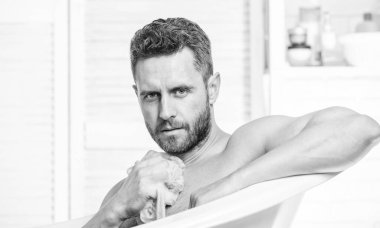 Küvette çıplak maço. Adam kaslı vücudu süngerle yıkıyor. Kişisel bakım. Banyodaki seksi adam. Köpüğü dikkatlice suyla yıka. Seks ve rahatlama konsepti. Temiz ol..