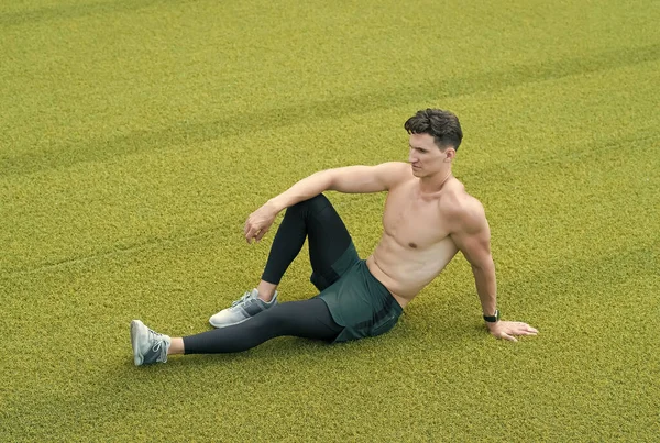 Een gespierde kerel laat op gras zitten. Shirtloze sportman rustend na het sporten. Een man die op gras zit. Ontspan je maar. sportief lifestyle concept. Ontspannen sexy topless man zitten op gras — Stockfoto