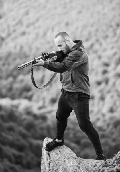 Concepto de caza furtiva. Hombre cazador furtivo brutal con fondo de paisaje natural arma. Caza ilegal. El cazador furtivo está al borde del acantilado. Hunter cazador furtivo buscando a la víctima. Hunter con rifle naturaleza ambiente — Foto de Stock