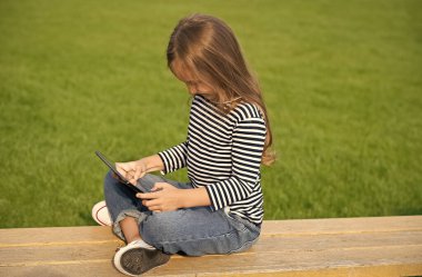 Dijital olarak senin. Küçük çocuk park bankında otururken tablet kullanıyor. Tablet bilgisayar teknolojisi. Modern hayat. Yeni teknoloji. Çevrimiçi oyun. Sosyal ağ. Sanal dünya. Eğlence ve eğlence teknolojisi
